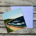 Card featuring an original artwork inspired by Huzzas, a much-loved surf break in Gracetown Bay, Western Australia, capturing the peaceful atmosphere and beauty of this special corner of the Margaret River coast. Styled on a rustic gray wooden background with a white envelope behind it.