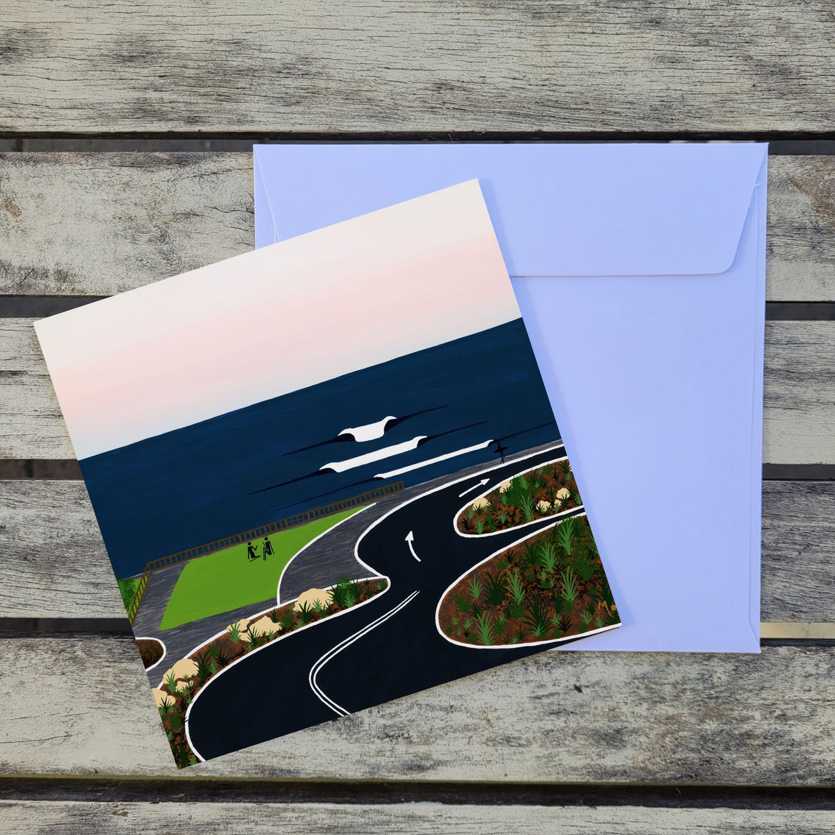 A square card featuring an original artwork inspired by Surfers Point in Prevelly, one of Margaret River's most famous surf spots and a special place to watch the waves, enjoy the sunset and spend time overlooking the Indian Ocean placed in front of a white envelope on a weathered wood surface.